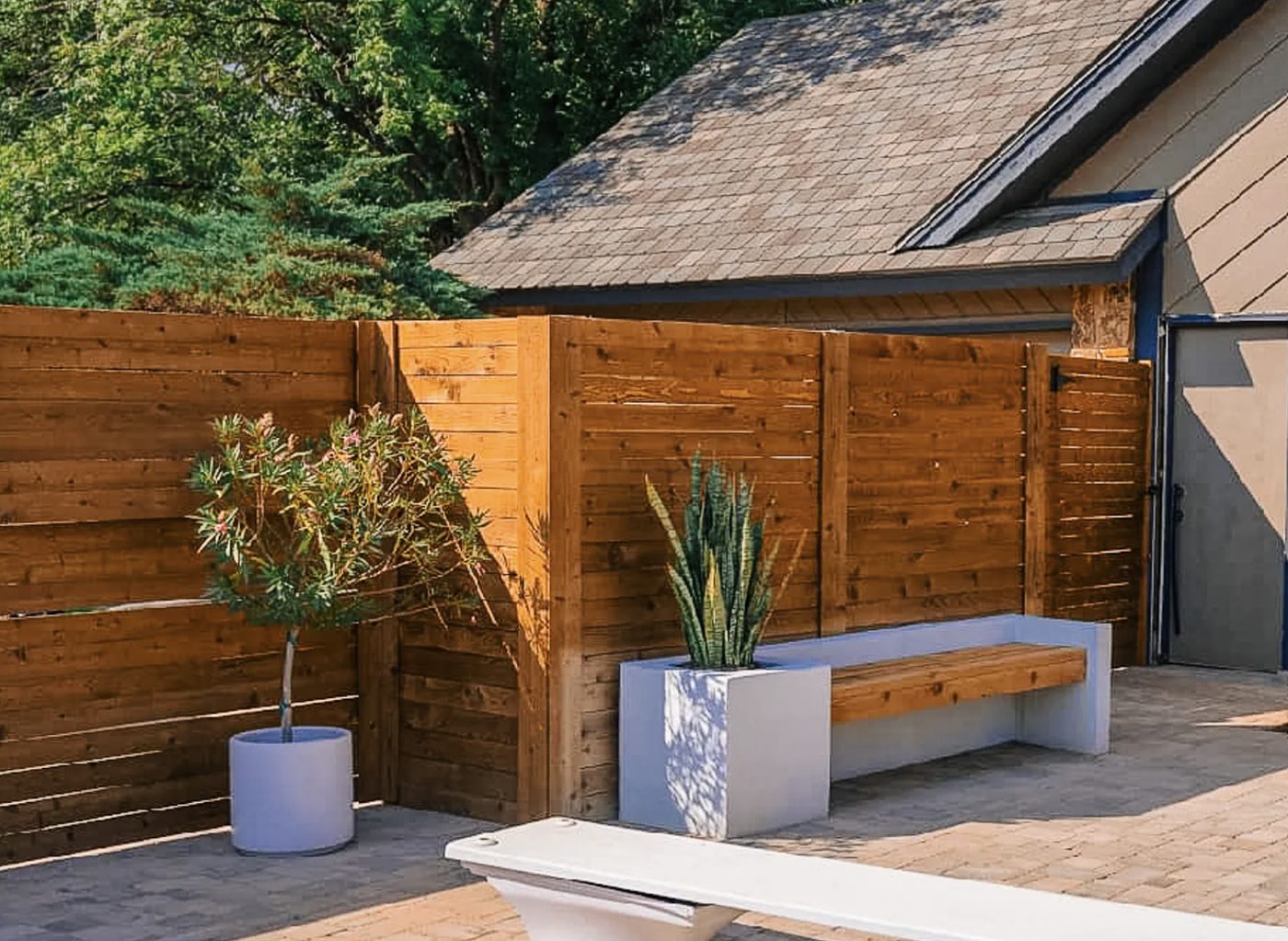 Horizontal cedar privacy fence with a built-in bench, concrete planters, and paver pool deck