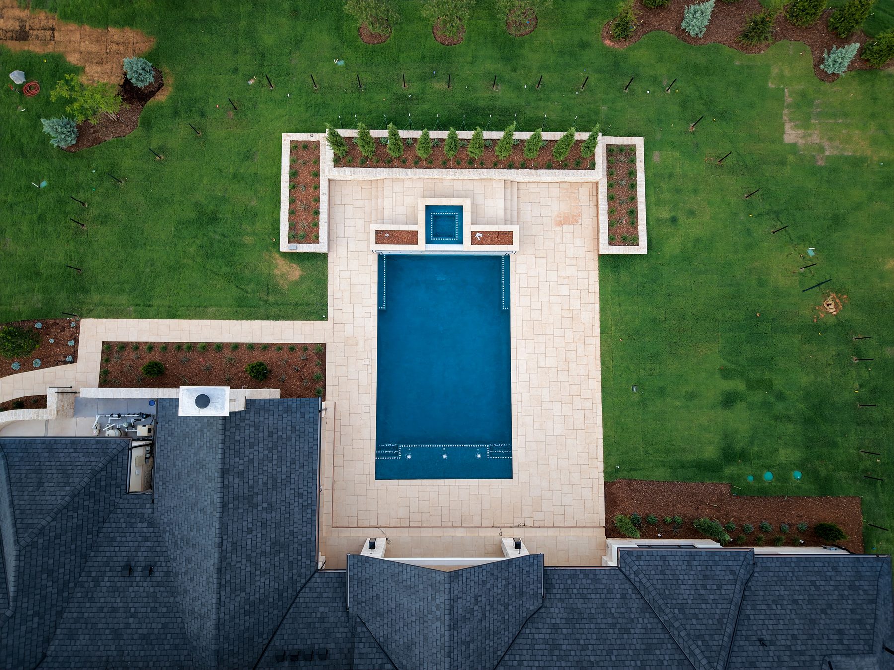 Overhead aerial view of a rectangular pool, limestone paver deck, raised planting beds, and newly landscaped lawn