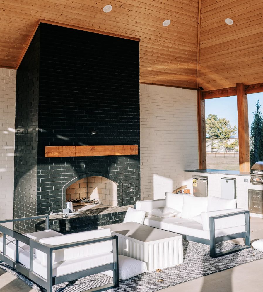 Outdoor kitchen and black brick fireplace inside a bright pavilion with a vaulted cedar ceiling