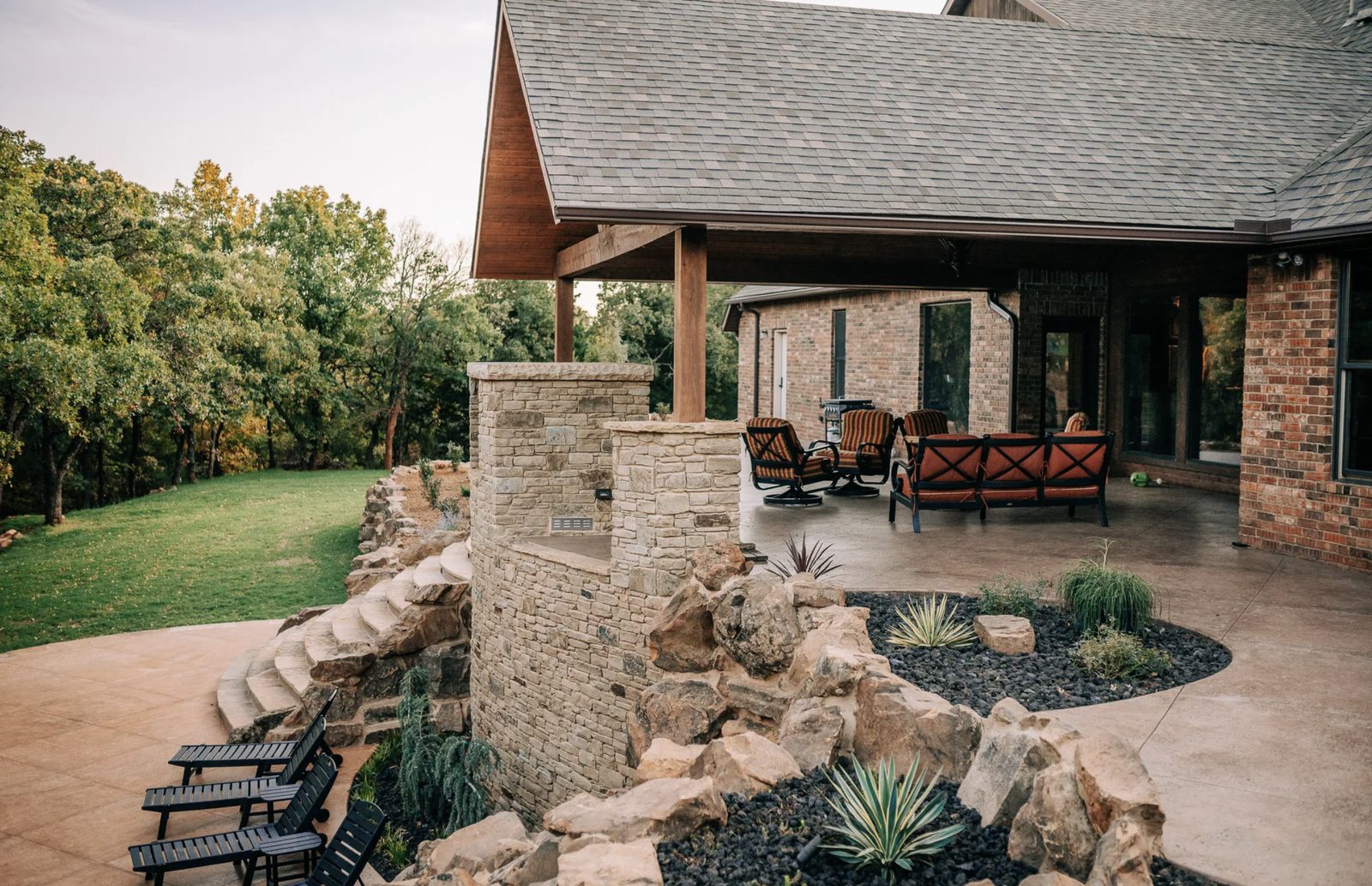 Curved natural stone retaining wall and sweeping stone staircase connecting a covered patio to a lower lawn